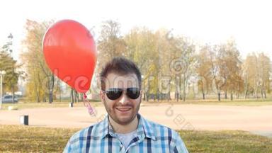 一个戴着黑色眼镜的时髦<strong>青年</strong>站着，手里拿着红色的气球，微笑着，一个节<strong>日</strong>的惊喜，慢动作